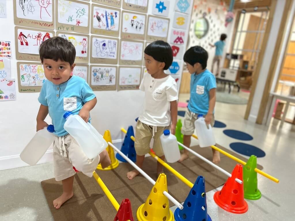 เด็กสองคนกำลังเล่นของเล่นพลาสติกสีสันสดใสบนพื้น ภายในห้องที่สว่างและบรรยากาศร่าเริง