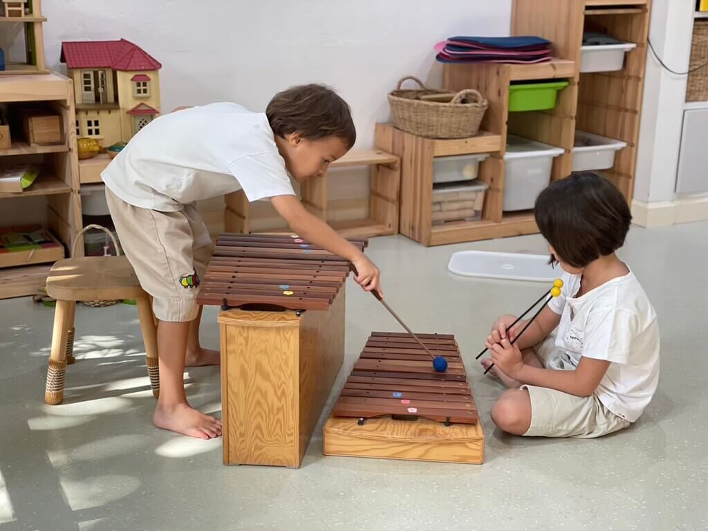 ผู้หญิงคนหนึ่งคุกเข่าอยู่บนพื้น กำลังมีส่วนร่วมทำกิจกรรมกับกลุ่มเด็ก ๆ ที่นั่งล้อมรอบเธออย่างตั้งใจ