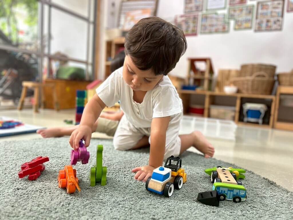 เด็กชายตัวน้อยกำลังเล่นอย่างตั้งใจ โดยต่อบล็อกของเล่นสีสันสดใสภายในห้องเรียนที่สว่างสดใส